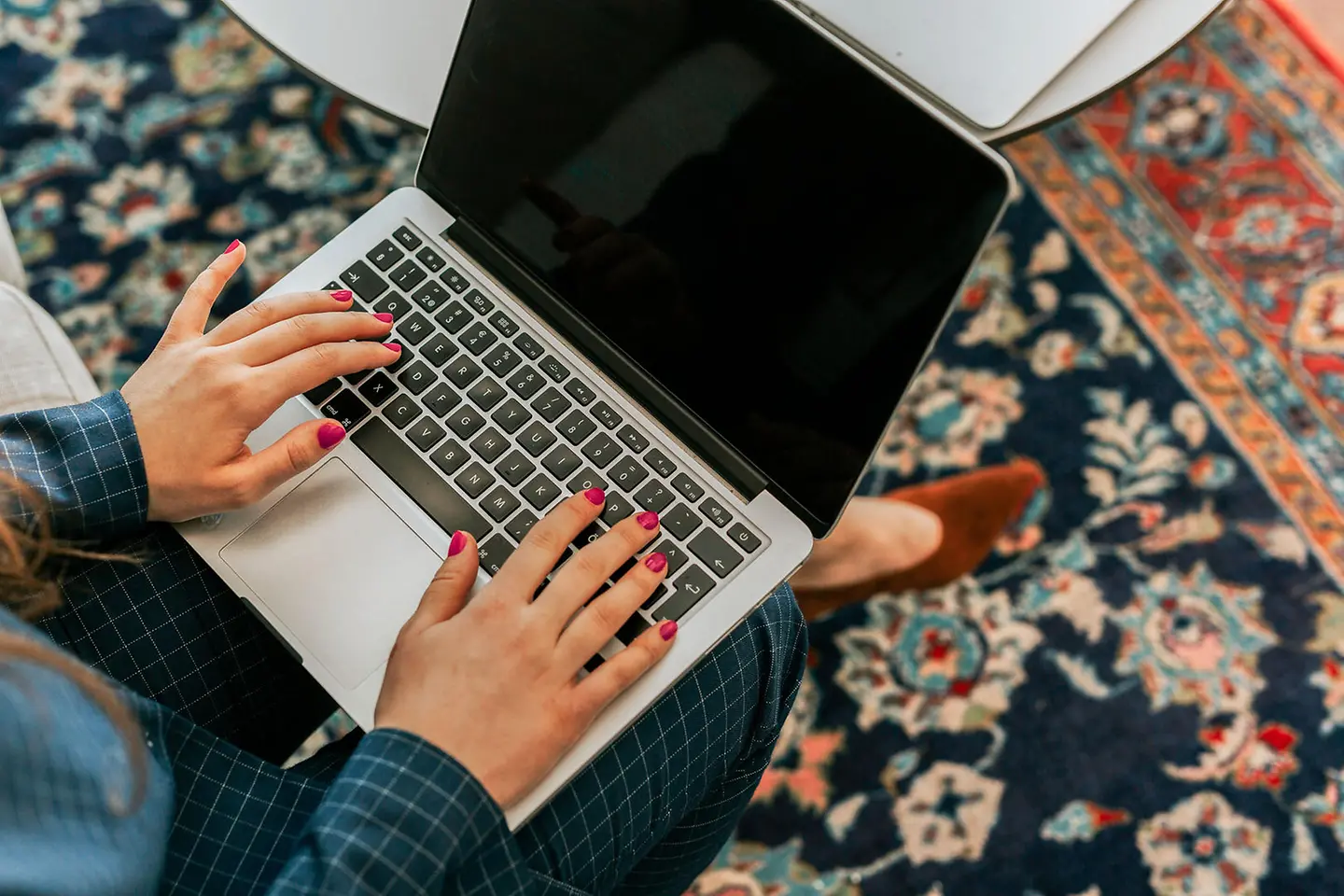 A woman is sitting on the carpet and working on her laptop