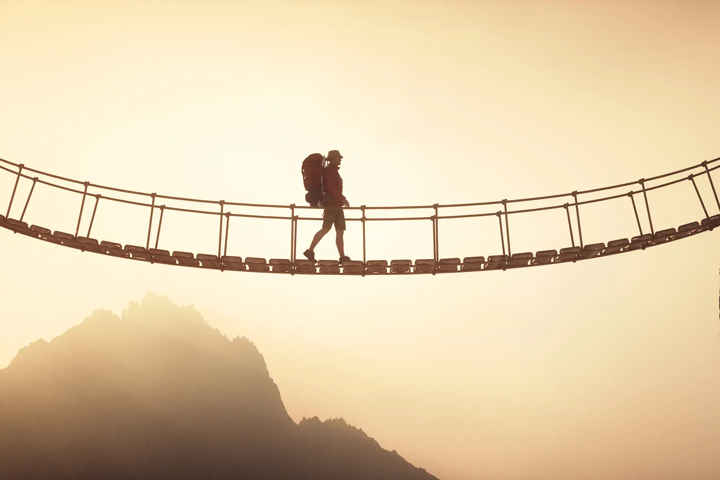 Ein Wanderer überquert eine Hängebrücke, die zwei Berggipfel verbindet