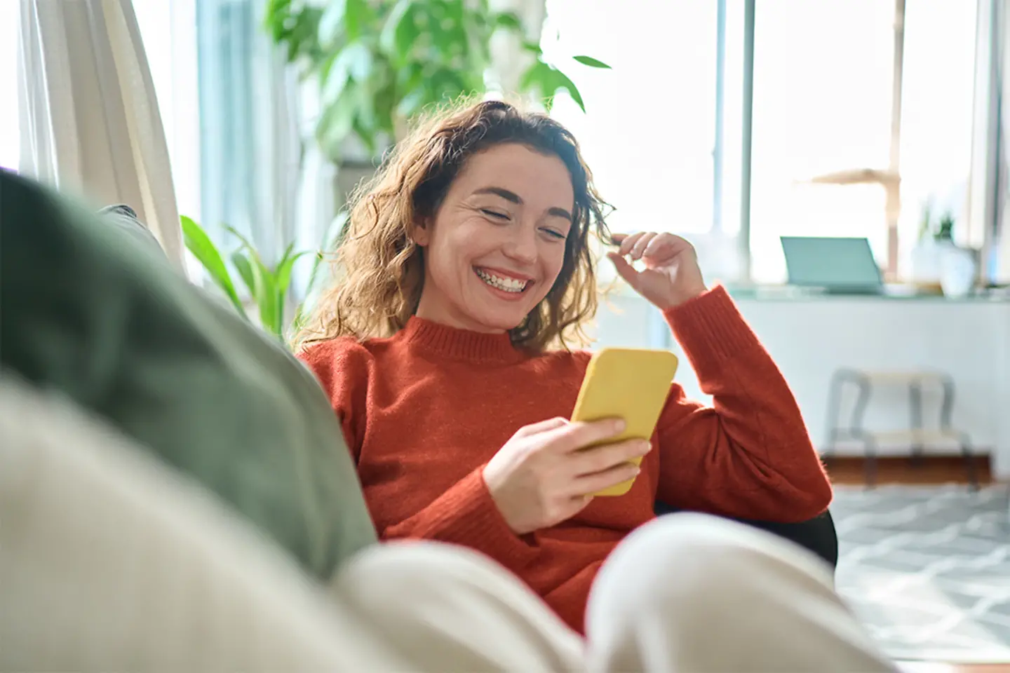 Young woman smiling while sitting on a sofa and using her smartphone