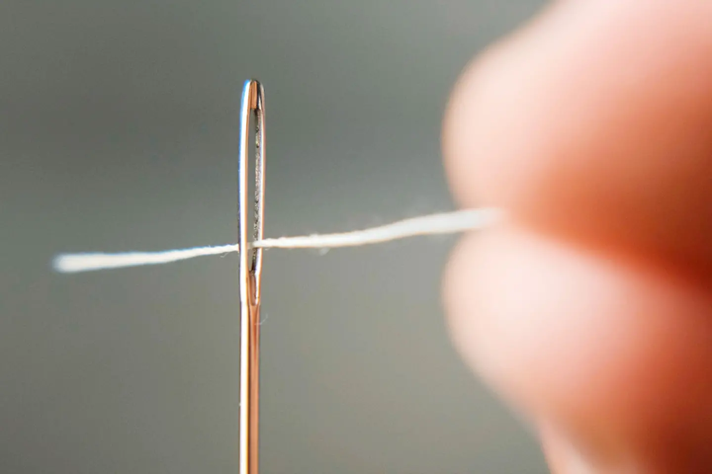 Macro shot of a hand threading a white thread through the eye of a needle