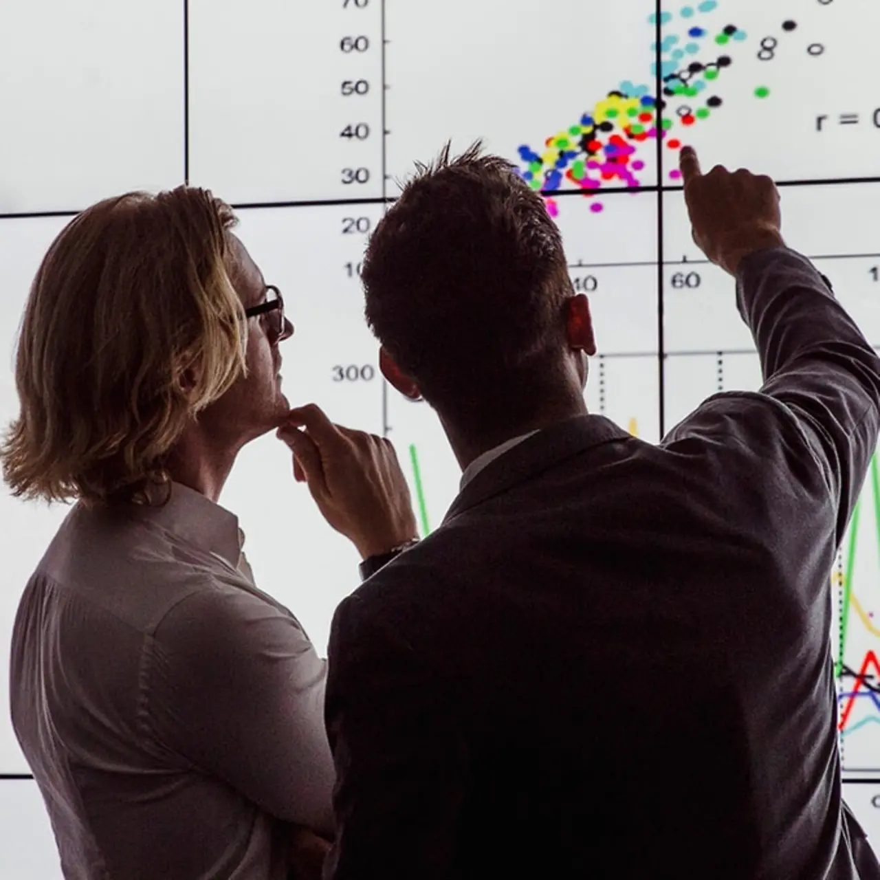 Zwei Menschen analysieren Daten vor großem Bildschirm